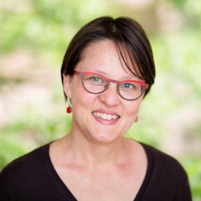 Photograph of Devi Stuart-Fox, smiling at the camera, with a blurred green and brown background.